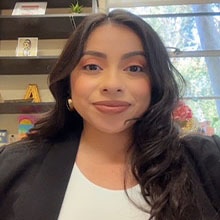 Woman with long wavy brown hair black blazer and white top in office